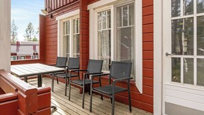 En träveranda med ett bord och stolar, en dörr och fönster.