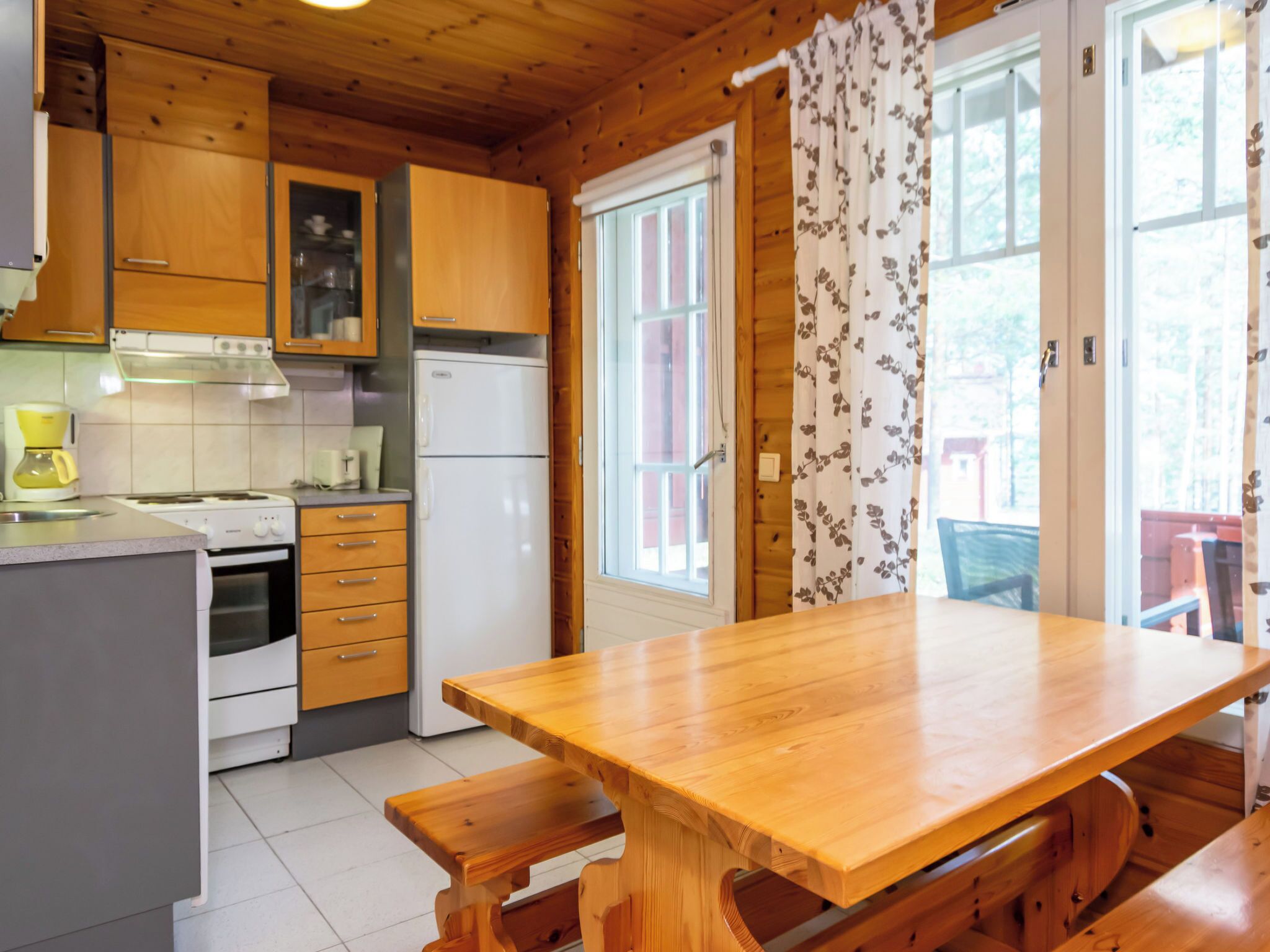 Une cuisine avec des meubles de rangement en bois, un réfrigérateur, une cuisinière et une table à manger en bois, accompagnée de bancs.