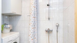 Un bagno con lavatrice, doccia con soffione a mano e parete rivestita in piastrelle.