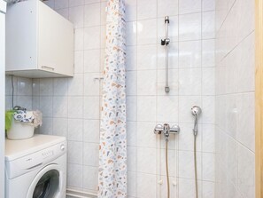 Un baño con lavadora, ducha con cabezal de ducha manual y pared de azulejos.