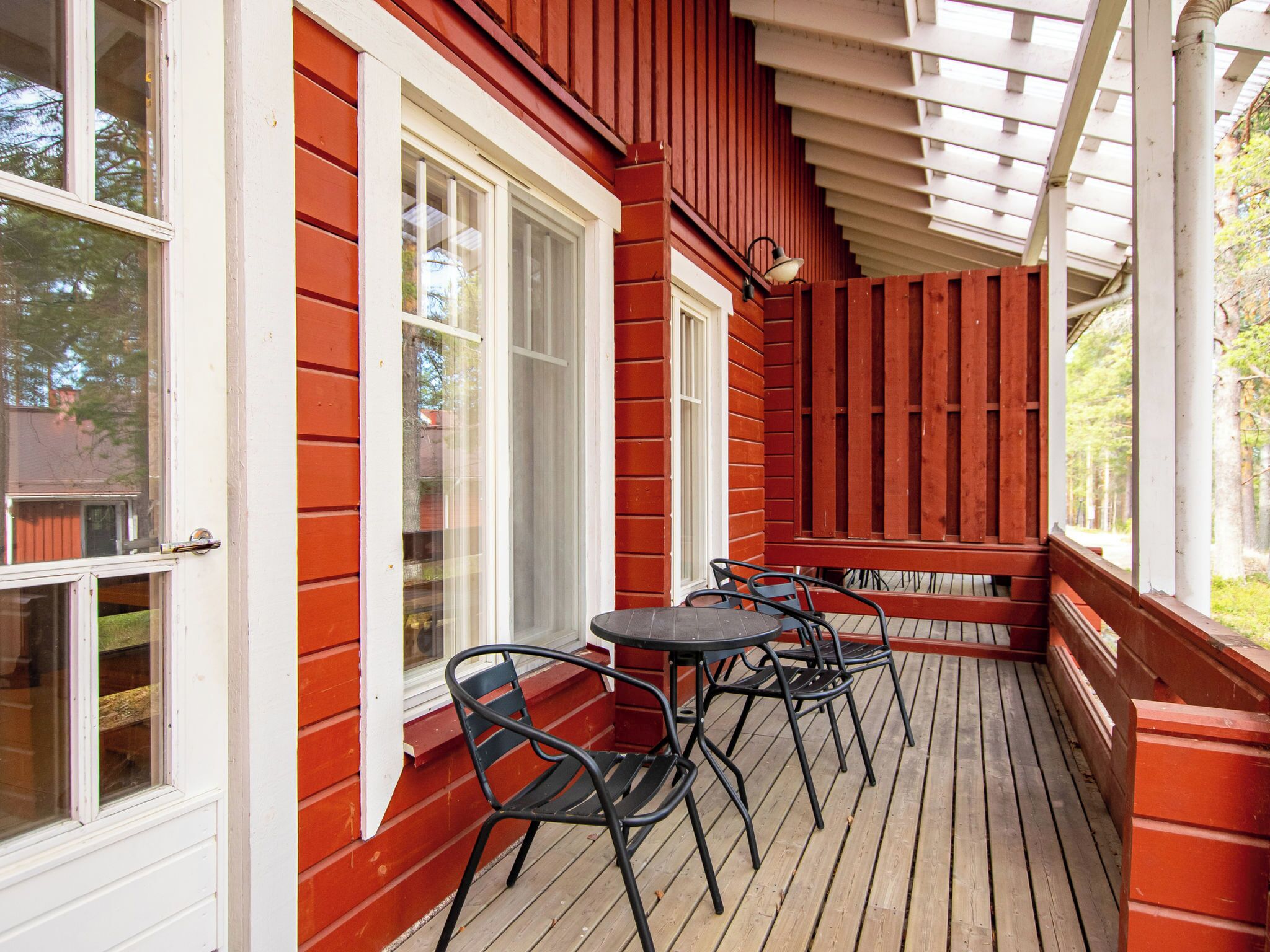 A covered outdoor area with a wooden deck, white-framed windows, and a table with chairs.