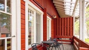 Un'area esterna coperta con un pavimento in legno, finestre con cornice bianca e un tavolo con sedie.