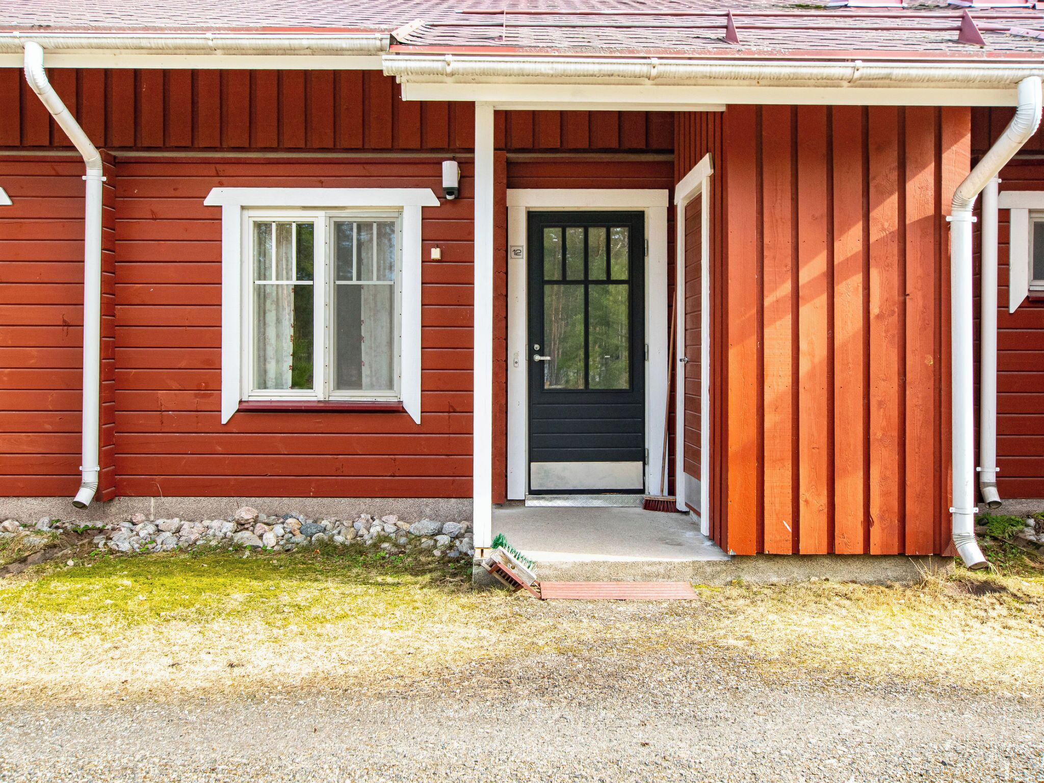 Une maison en bois rouge avec une porte noire, des encadrements de fenêtres blancs et un petit porche.
