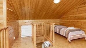 Ein Holzhütten-Interieur mit einem Etagenbett, einem kleinen weißen Schminktisch und einer schrägen Decke mit einer Leuchte.