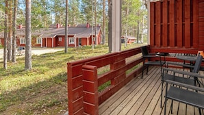 Eine Holzterrasse mit Sitzgelegenheiten im Freien mit Blick auf ein bewaldetes Gebiet mit roten Gebäuden.