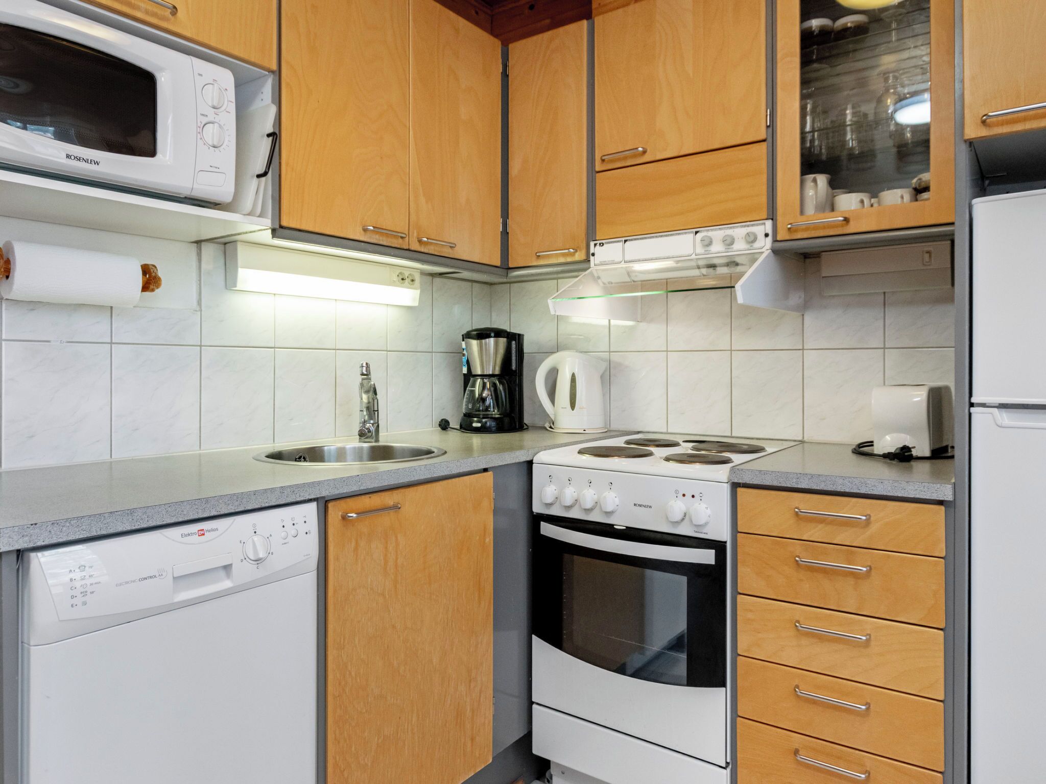 A kitchen with a microwave, stove, coffee maker, kettle, and dishwasher.