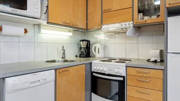 A kitchen with a microwave, stove, coffee maker, kettle, and dishwasher.