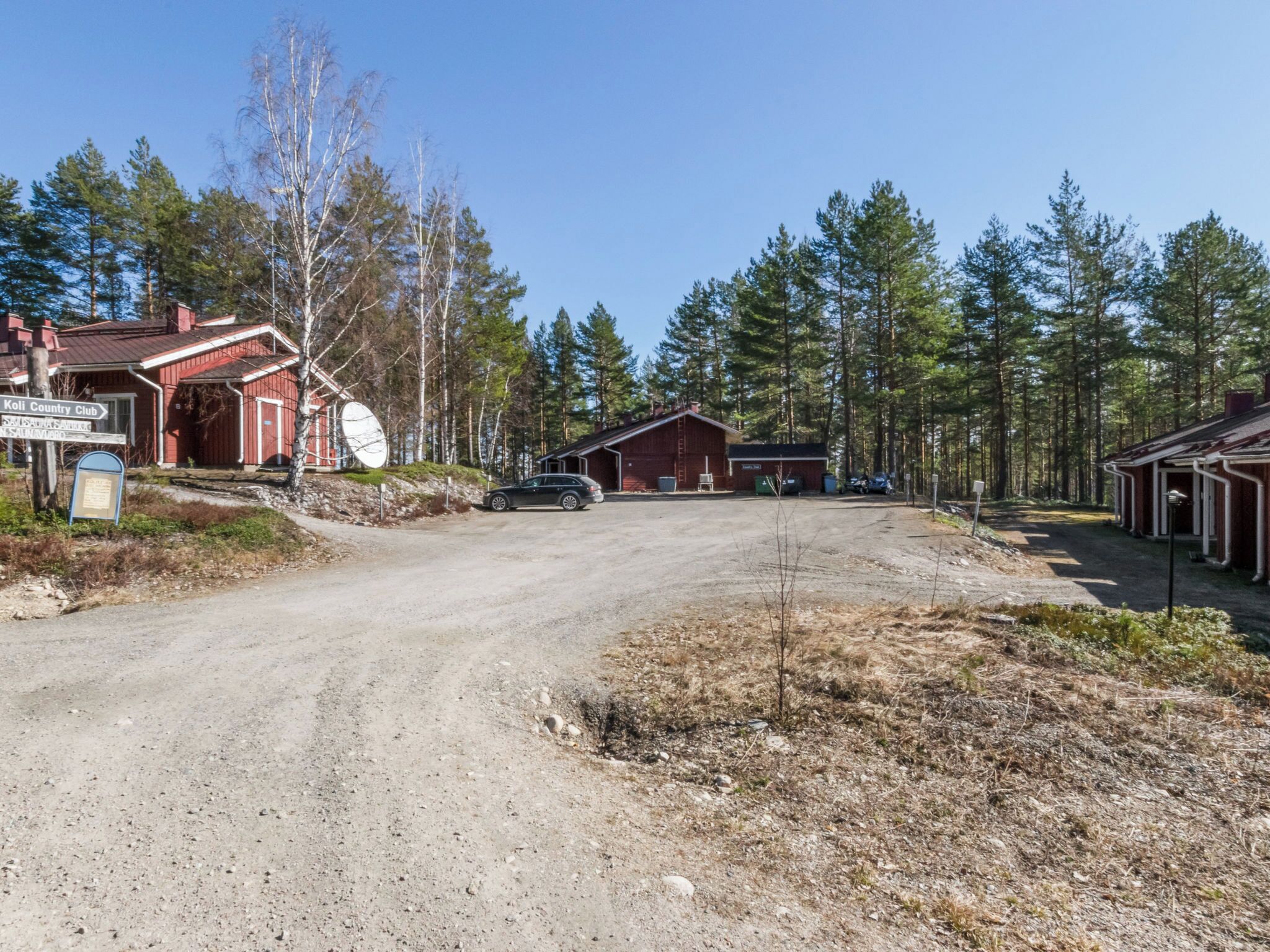 Maalaismaisemassa kulkeva tie johtaa punaiseen rakennukseen, jonka edessä on kyltti, jossa lukee Koli Country Club.