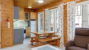 A wooden cabin interior with a kitchen, dining area, and a sofa.
