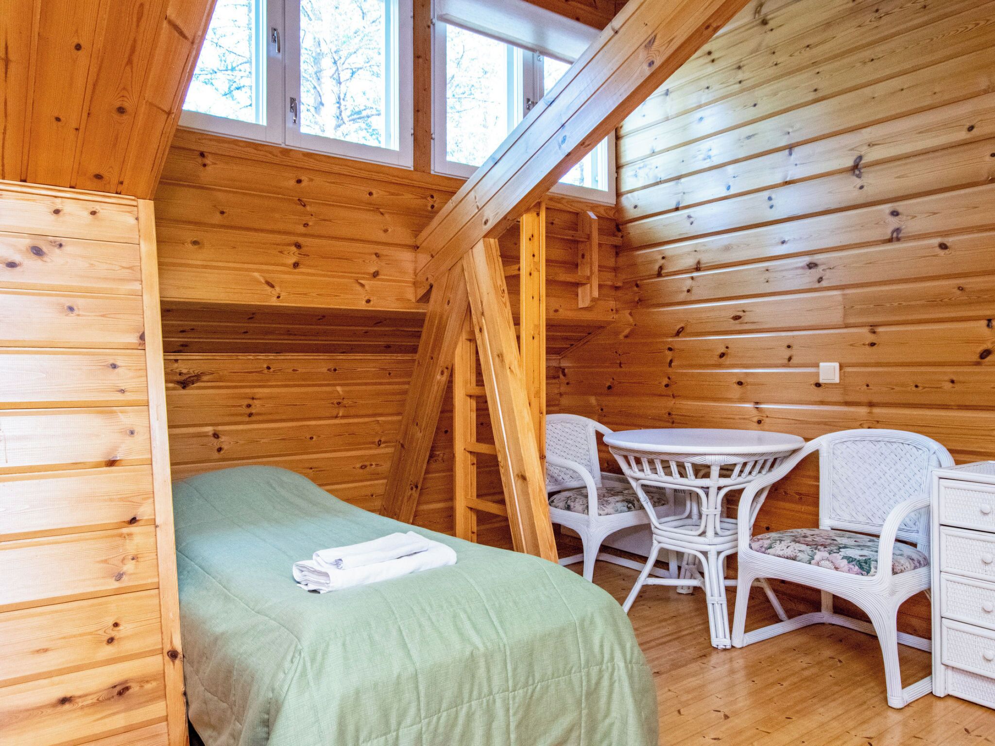 Una habitación tipo cabaña de madera con cama altillo, una mesita, dos sillas y una escalera.