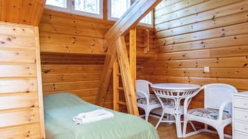 Una habitación tipo cabaña de madera con cama altillo, una mesita, dos sillas y una escalera.