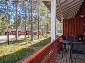 Puinen terassi, jossa on ulkotilaa istumiseen, ja josta avautuu näkymä metsäiselle alueelle, jossa on myös mökkejä.