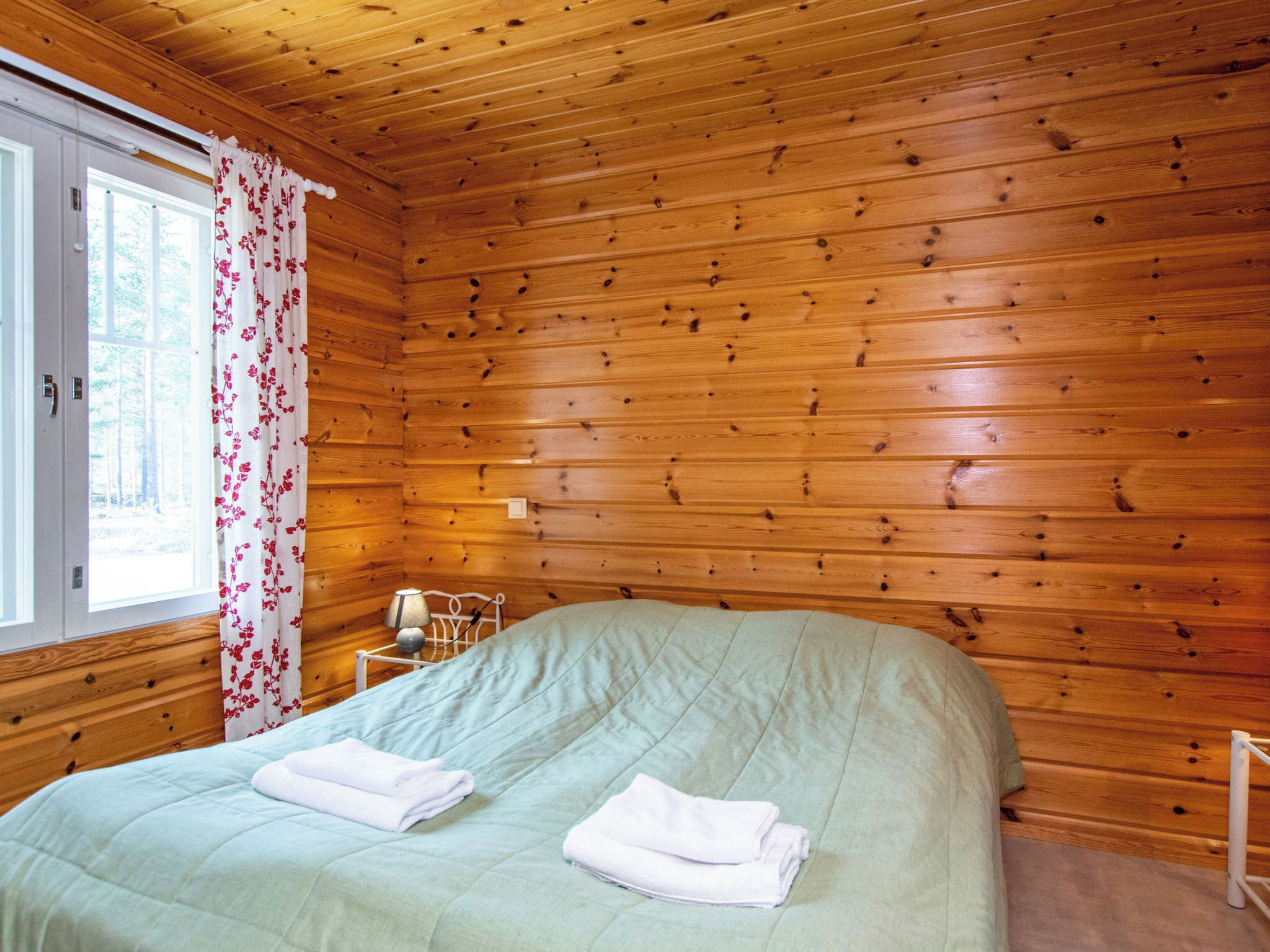 Ein Zimmer mit Holzwänden, einem Bett mit grüner Bettdecke, einem weißen Kopfkissen und einem weißen Handtuch auf dem Bett.