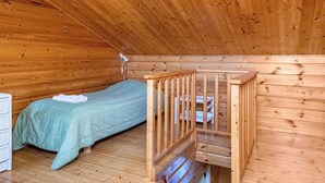 Une petite cabane d’une seule pièce, avec un plafond en bois, un lit, une petite table et une commode blanche.