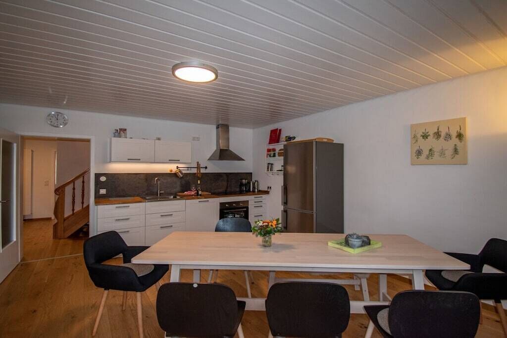 Eine moderne Küche mit weißen Schränken, einem Edelstahlkühlschrank und einem Essbereich mit einem Holztisch und Stühlen.