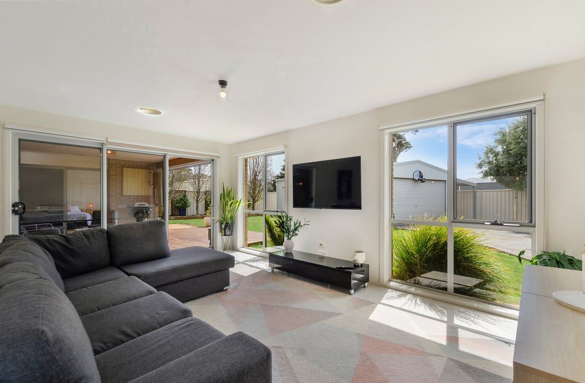 A modern living room with a sectional sofa, a flat-screen TV mounted on the wall, and a sliding glass door leading to an outdoor area.