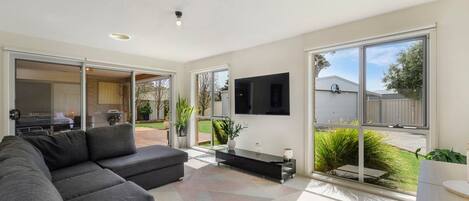 A modern living room with a sectional sofa, a flat-screen TV mounted on the wall, and a sliding glass door leading to an outdoor area.