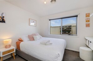A bedroom with a bed, bedside table, lamp, and a window with a view of buildings.