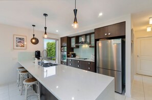 A modern kitchen with a large island, stainless steel appliances, and pendant lighting.