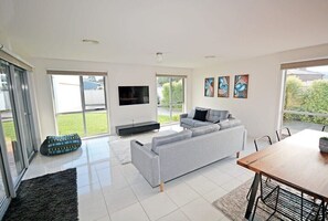 A modern living room with a grey sofa, a flat-screen TV, and a dining table with chairs.
