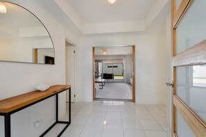 A hallway with a wooden console table, a large mirror, and a door leading to a room with a bed and a desk.