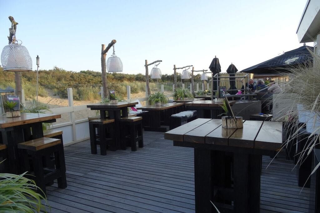 An outdoor deck with wooden tables and benches, surrounded by decorative lanterns and potted plants.
