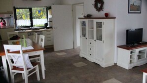A compact living space with a dining area, a kitchen with a window, a white cabinet, and a television.