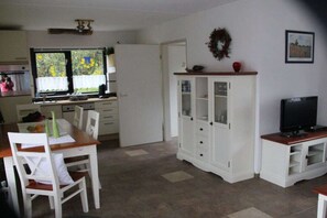 A compact living space with a dining area, a kitchen with a window, a white cabinet, and a television.