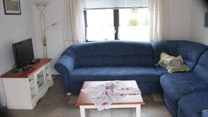 A living room with a blue sofa, a television on a wooden stand, and a table with a cloth.