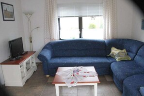 A living room with a blue sofa, a television on a wooden stand, and a table with a cloth.