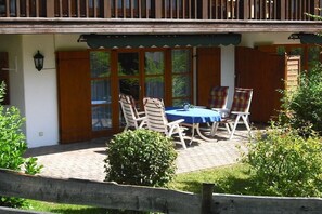 Un patio techado al aire libre con mesa y sillas, cerca de madera y follaje.