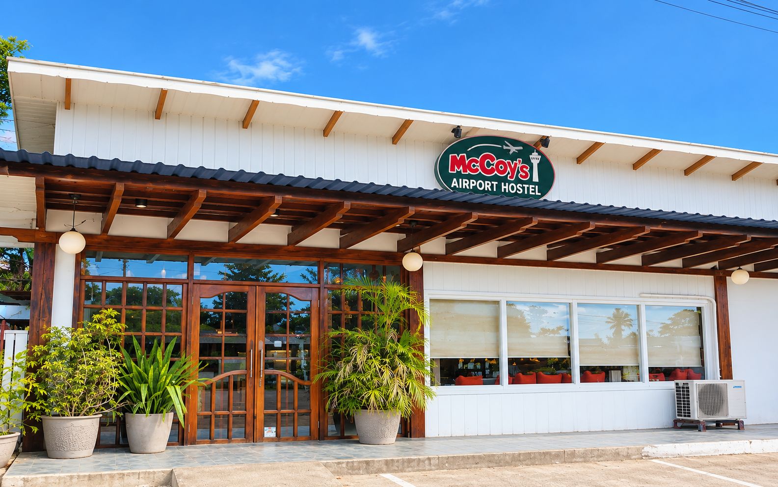 A McCoy's Airport Hostel with a wooden facade, large windows, and potted plants in front.