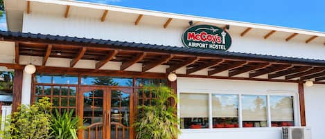 Un hostal McCoy's cerca del aeropuerto, con fachada de madera, ventanas grandes y plantas en macetas al frente.