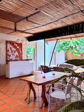 Un comedor con mesa y sillas de madera, pared de ladrillo blanco y un ventanal con vistas a la vegetación.