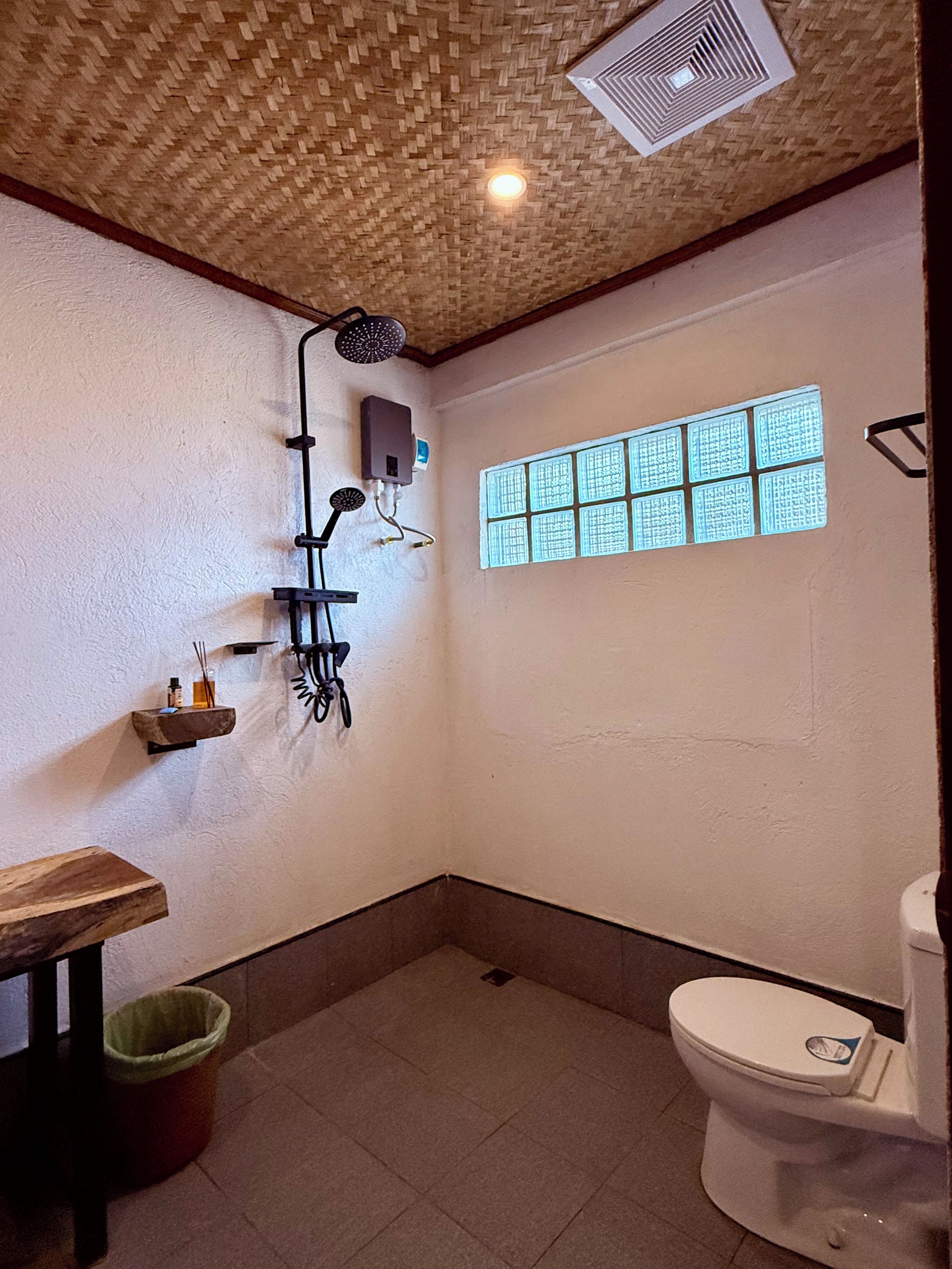 Un baño con ducha, inodoro, ventana con diseño de celosía y ventilador de techo.