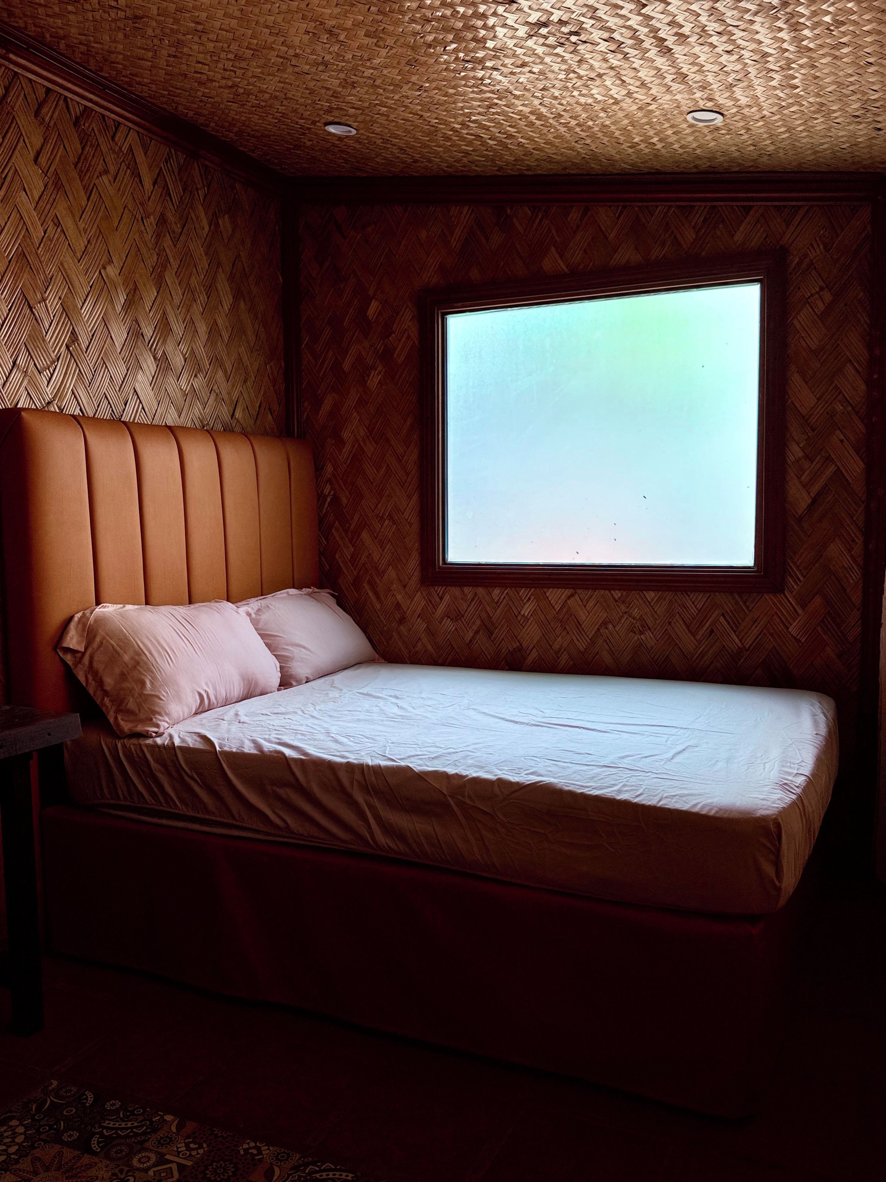 A single bed with a headboard, a window, and a woven ceiling.