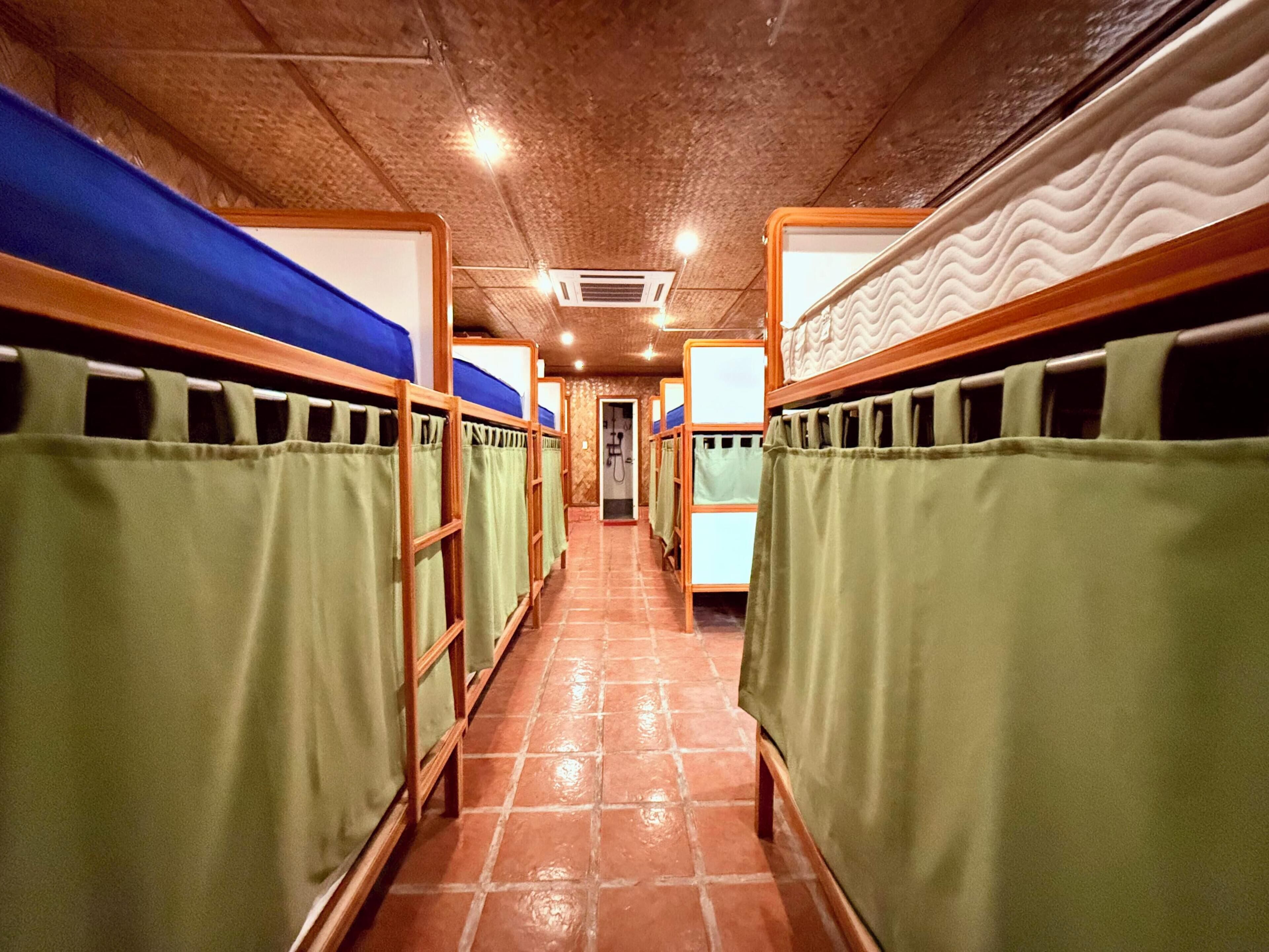 Un pasillo con literas, cada una con una cortina verde, que conduce a una puerta al final.