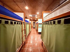 Un pasillo con literas, cada una con una cortina verde, que conduce a una puerta al final.