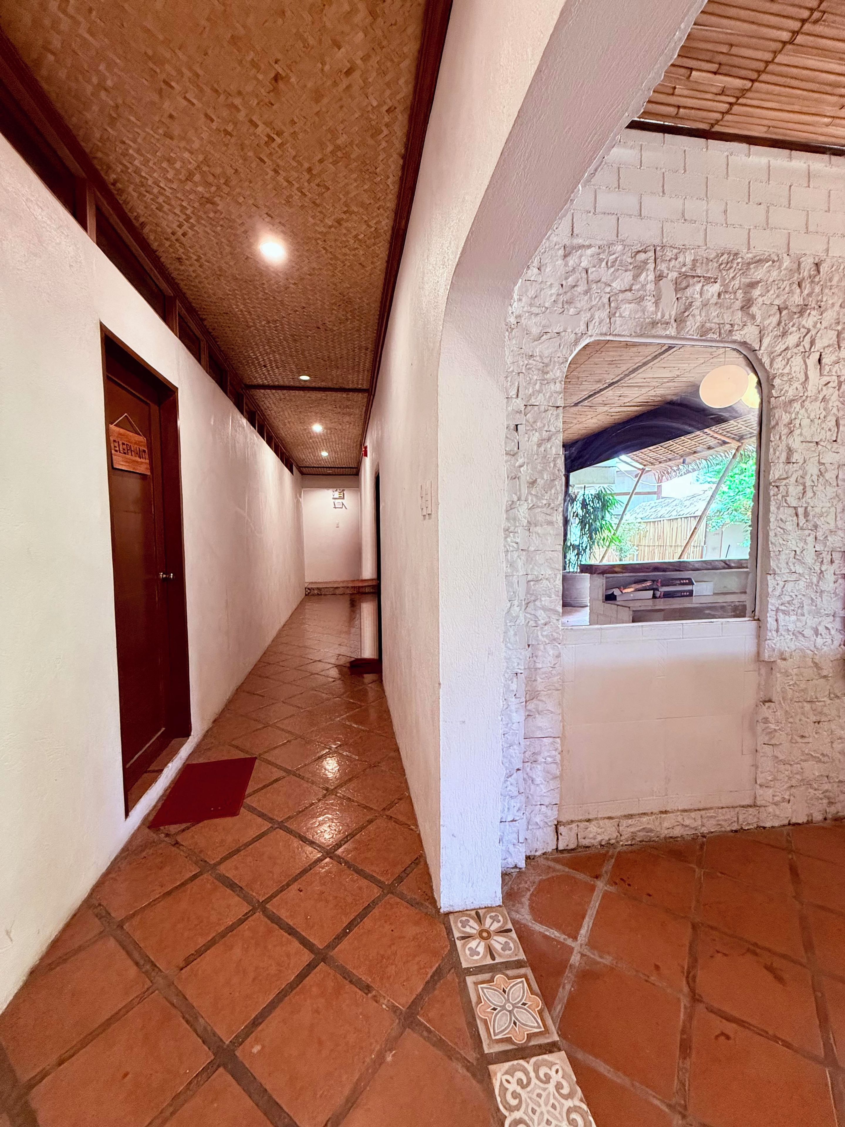 Un pasillo con piso de baldosas, una puerta de madera con un letrero y una pared de piedra con una ventana.