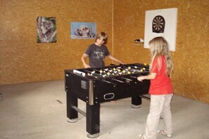 Ein Zimmer mit einer Kicker-Tischfußballplatte, einer Dartscheibe und zwei gerahmten Bildern an der Wand.
