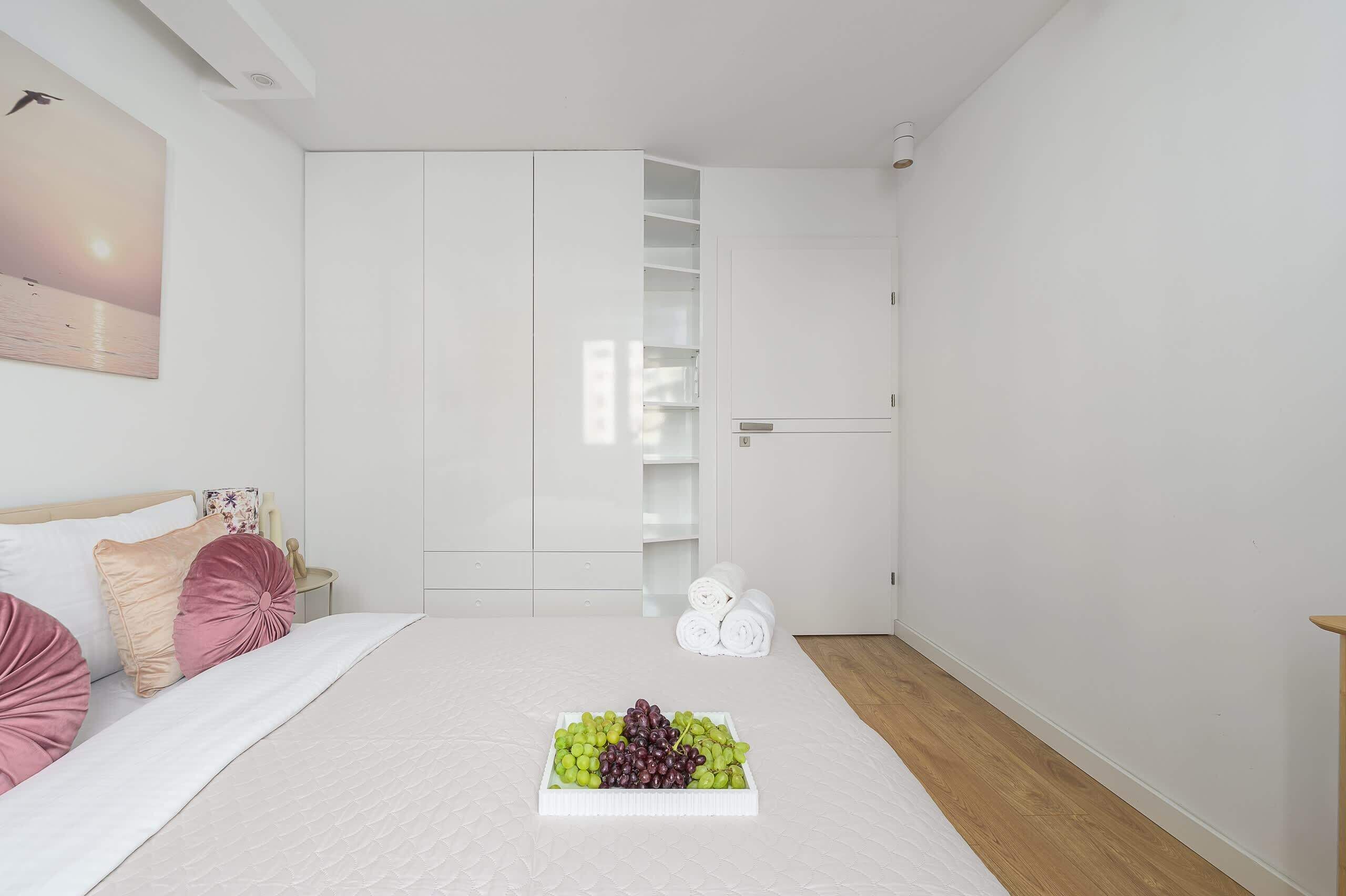 Une chambre à coucher avec un lit, une table de chevet, une armoire et une assiette de raisins.