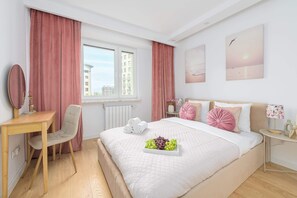 Una camera da letto moderna con un letto, una scrivania e una sedia. Si nota una finestra con tende, un termosifone e un quadro appeso al muro.