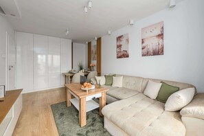 Ein modernes Wohnzimmer mit einem Holzesstisch, einem beigefarbenen Sofa und einem grünen Teppich.