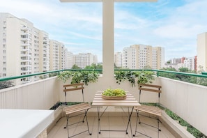 Ein Balkon mit Tisch und Stühlen, Topfpflanzen und Blick auf umliegende Gebäude.
