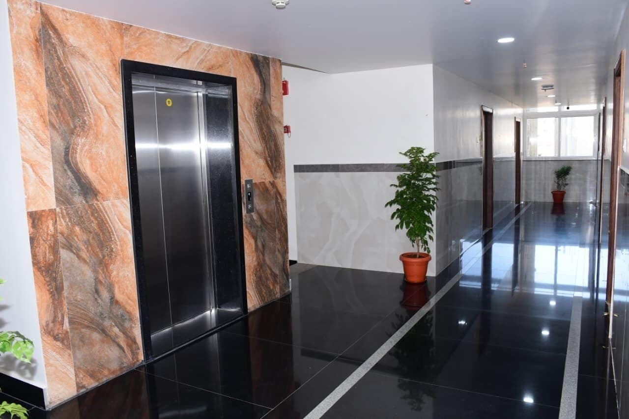 Un pasillo con pared de mármol, una planta en maceta y una puerta con un letrero.