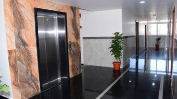 Un pasillo con pared de mármol, una planta en maceta y una puerta con un letrero.