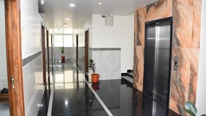 A hotel corridor with a polished floor, a potted plant, and an elevator. - P A R GRAND LUXURY HOTEL  (Anantapur)