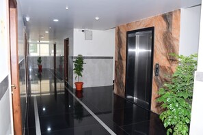 A modern hallway with a polished floor, a marble wall, and a potted plant. - P A R GRAND LUXURY HOTEL  (Anantapur)