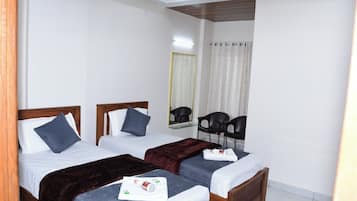 Habitación de hotel con dos camas individuales, un espejo, una silla y una mesita con una botella y una caja de pañuelos.