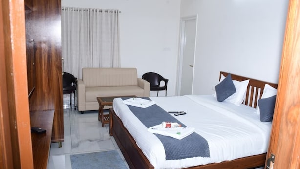 A hotel room with a bed, a sofa, a chair, and a wooden wardrobe. - P A R GRAND LUXURY HOTEL  (Anantapur)